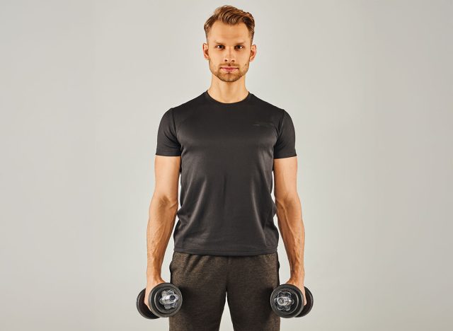 A young sportsman in active wear holding two dumbbells in front of a white background.