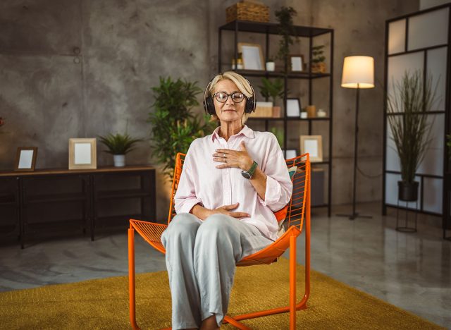 Mature woman sit on chair with headphones and have guided meditation