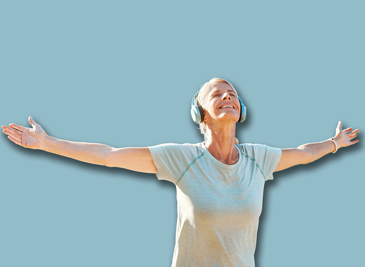 Woman, headphones or freedom on mountain outdoor for fitness achievement, exercise victory or workout goals. Mature, person and happy with hands raised on hill for training success with mockup space