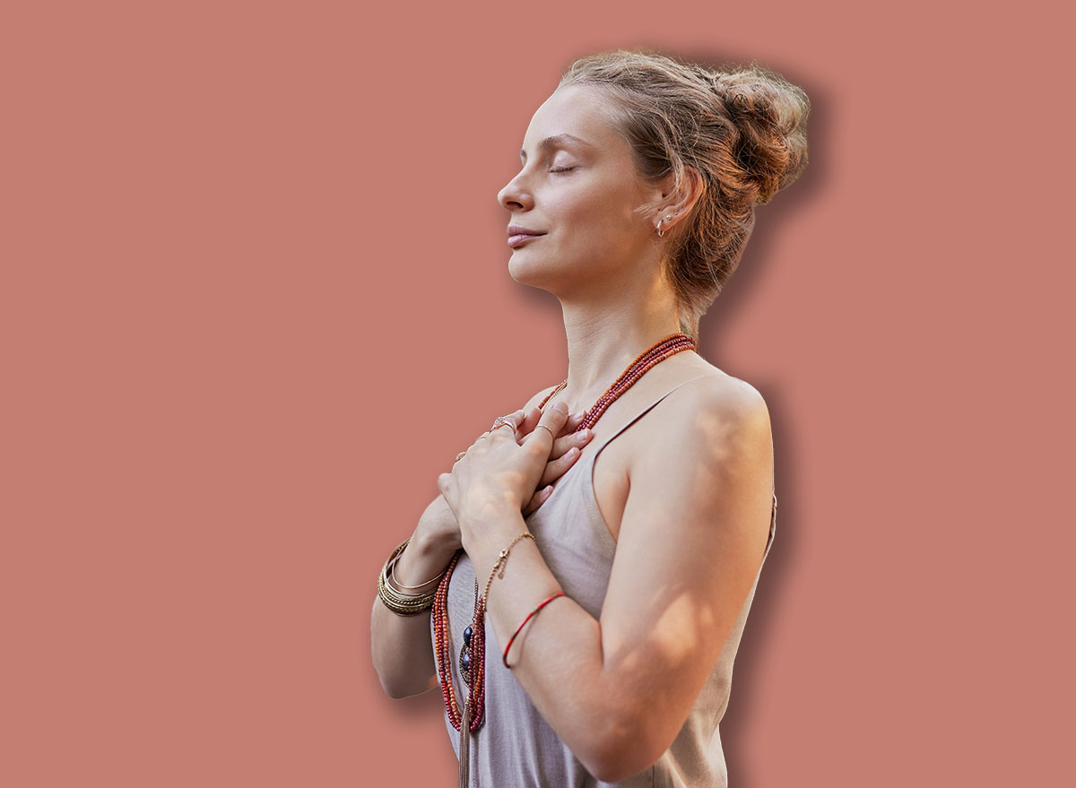 Group of people standing outdoors with hands on their hearts, practicing mindfulness in a wellness retreat. Young woman in a wellness retreat center connecting to inner peace during a healing session.