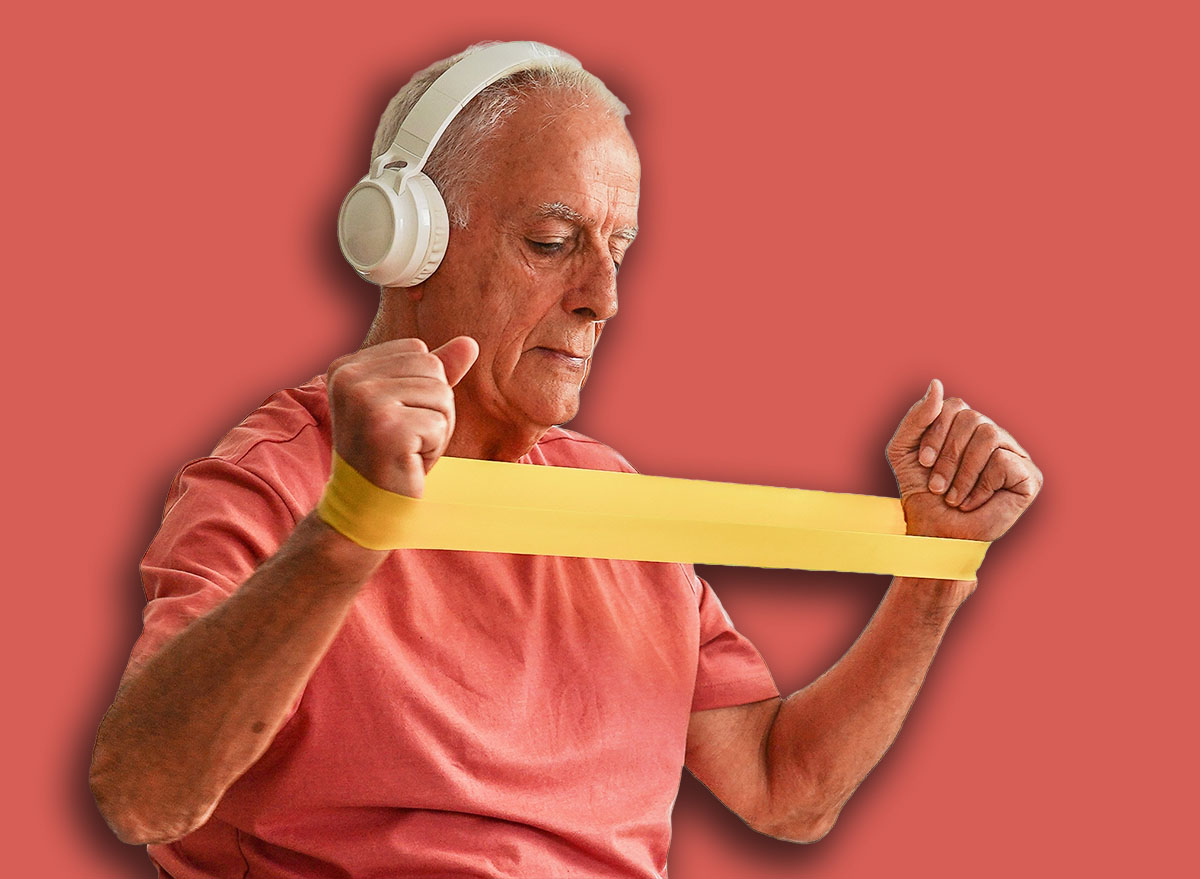 Elderly man exercising with elastic band at home following online fitness class on laptop