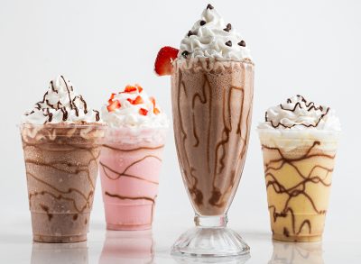 Four tempting milkshake variations: chocolate, strawberry, vanilla, and a mocha blend, each topped with whipped cream and chocolate drizzle