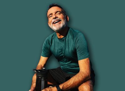 Mature male sitting by the water, smiling, enjoying nature during a sunny day outdoors.