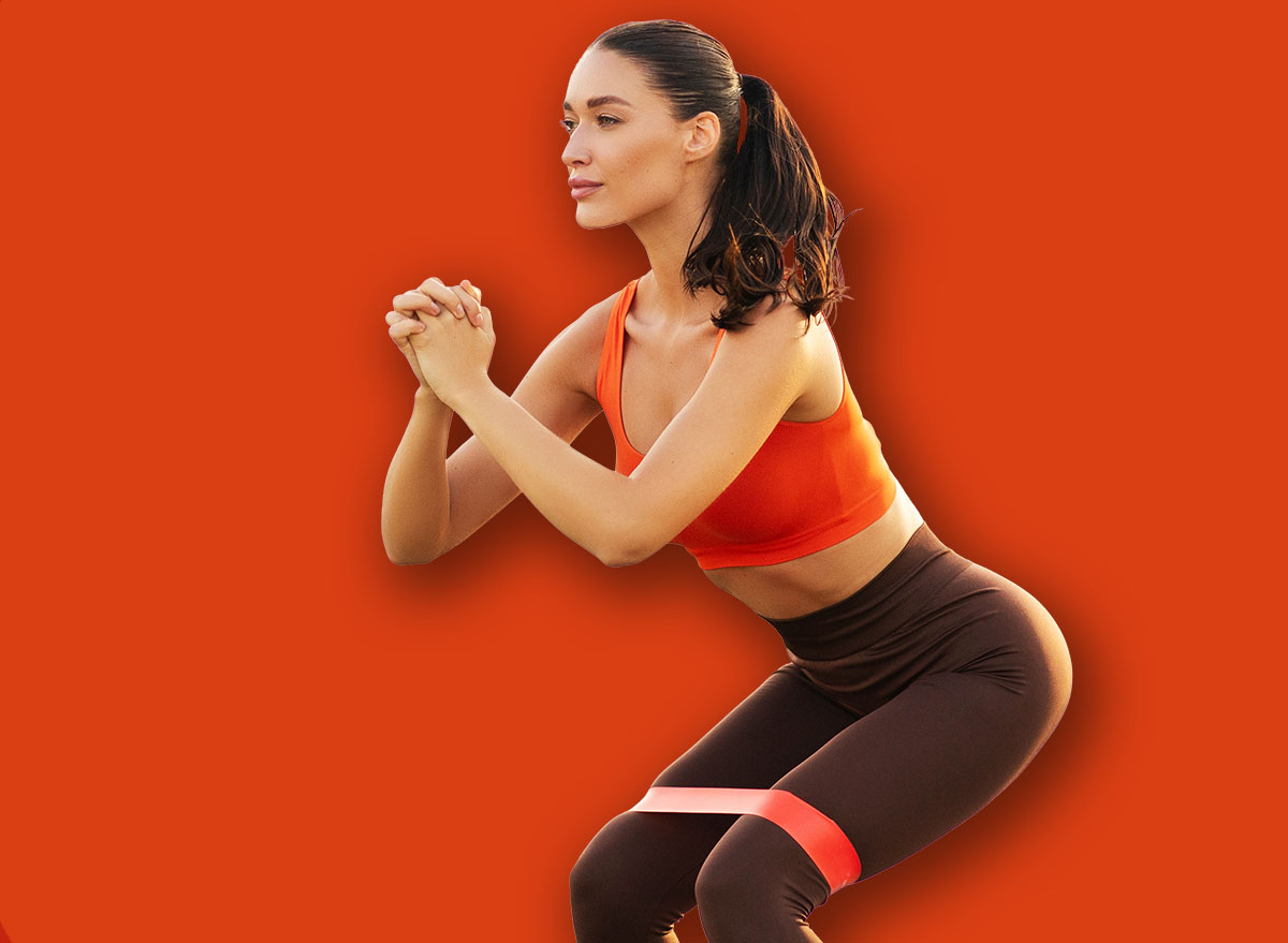 Fit lady in the squat position using resistance band for additional effort, having outdoors workout with breathtaking view of nature, copy space