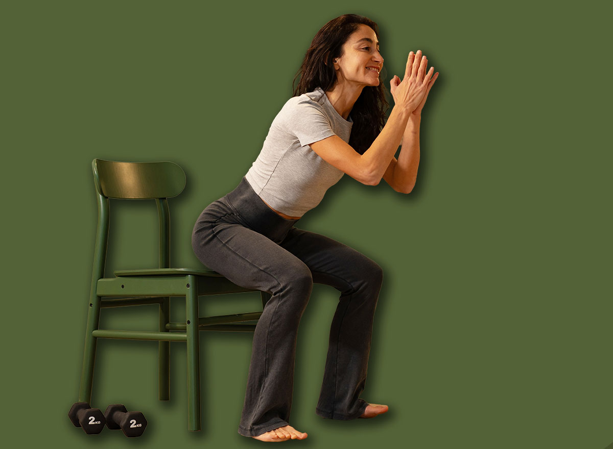 Smiling athletic woman performing chair squat exercise at home u