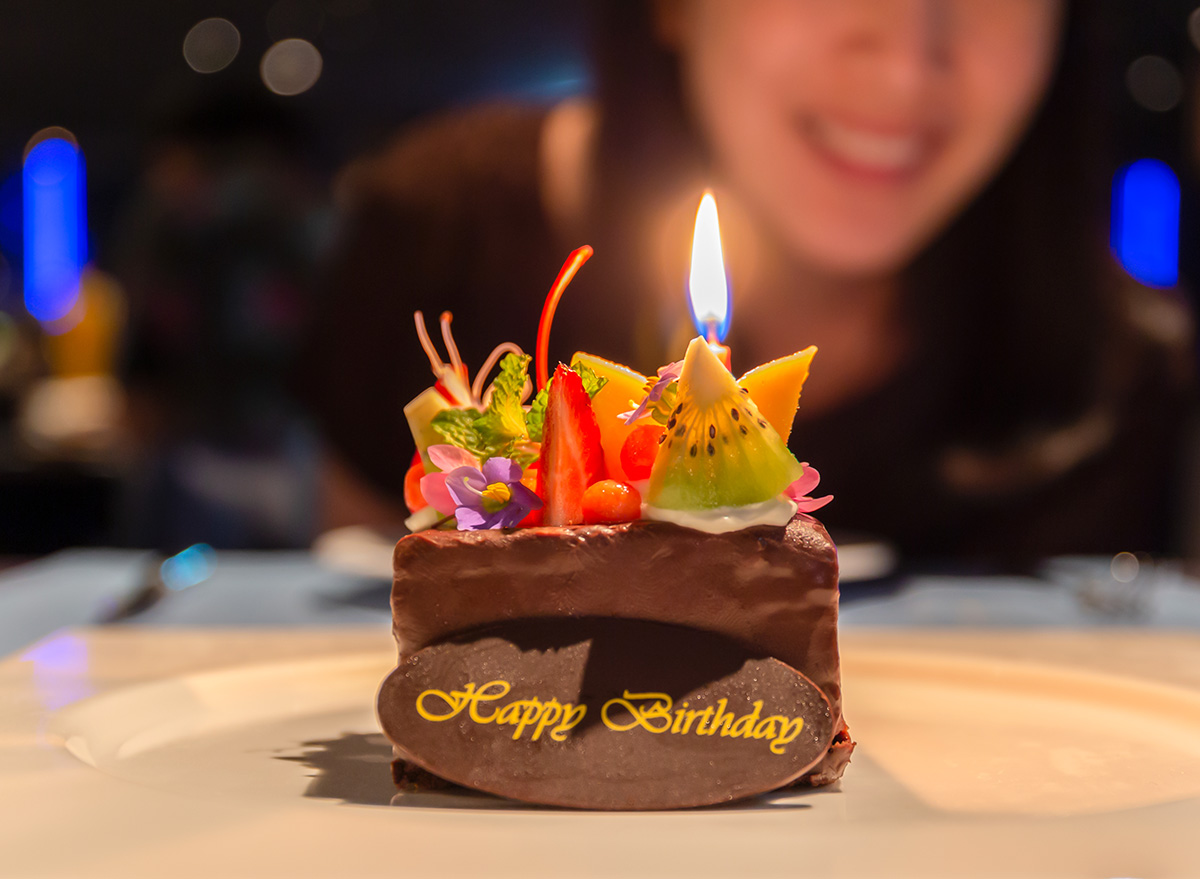 Woman celebrating birthday with chocolate fruit cake with candle lit