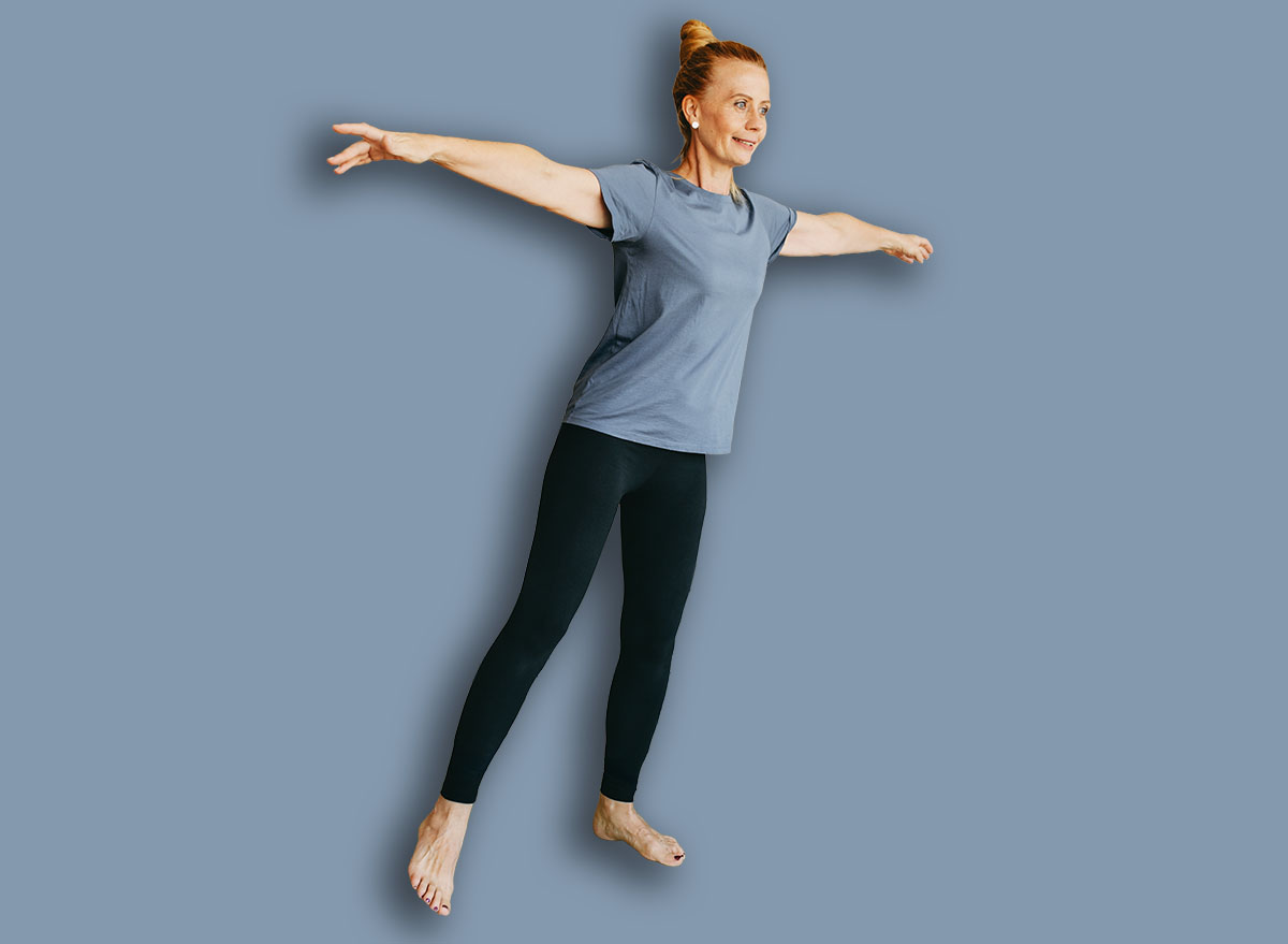 Smiling fit woman in sport clothes keeping body in good shape, having indoor training using resistance loop band, doing leg lifts, holding arms out of the side trying to catch balance