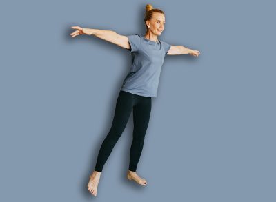 Smiling fit woman in sport clothes keeping body in good shape, having indoor training using resistance loop band, doing leg lifts, holding arms out of the side trying to catch balance