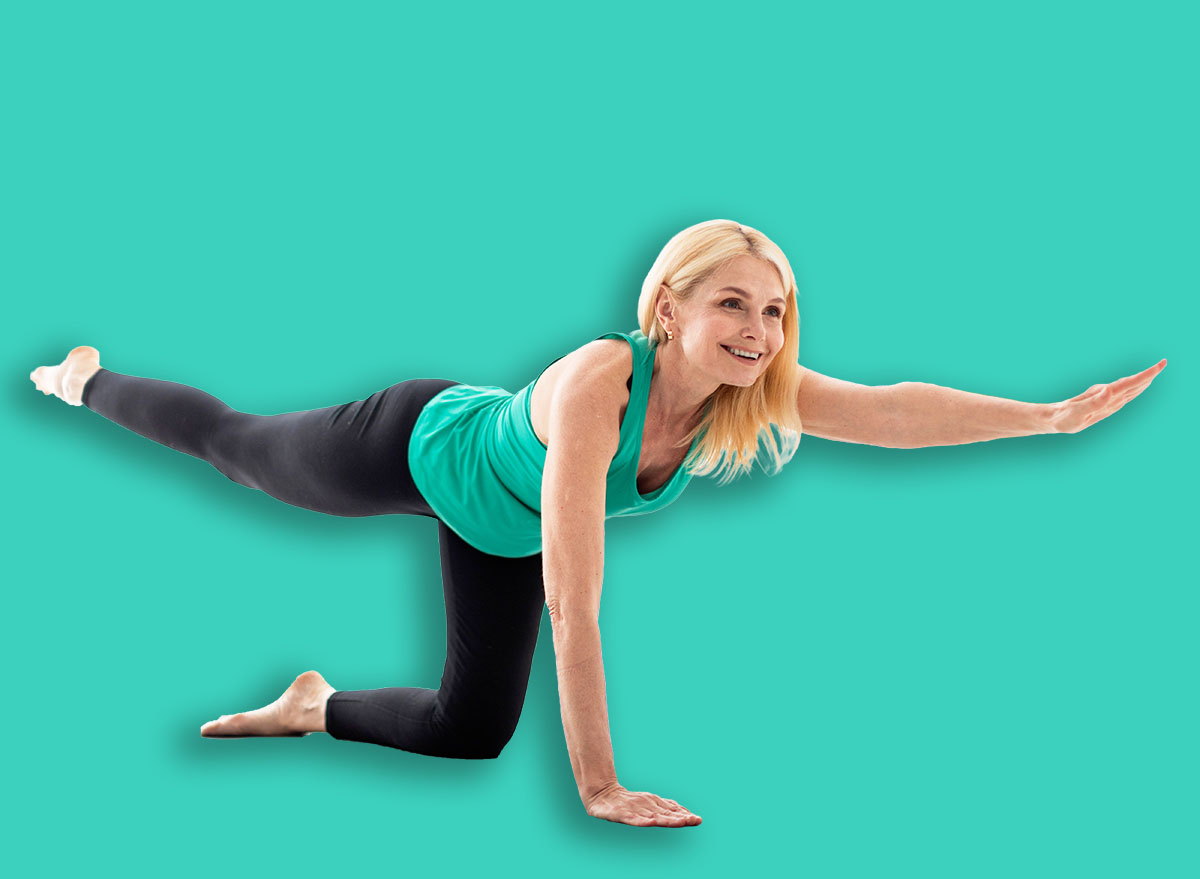 Beautiful mature lady in sportswear doing morning yoga, making bird dog pose, smiling senior woman training on fitness mat at home, stretching opposite leg and arm, enjoying healthy lifestyle