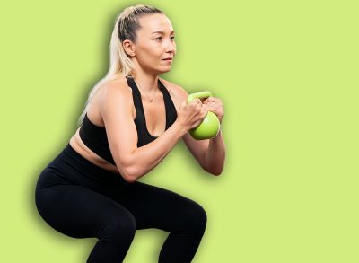 Athletic and sporty senior woman engaging in leg day training session with squat and bodyweight kettle ball at home exercise as concept of healthy fit body lifestyle after retirement. Clout