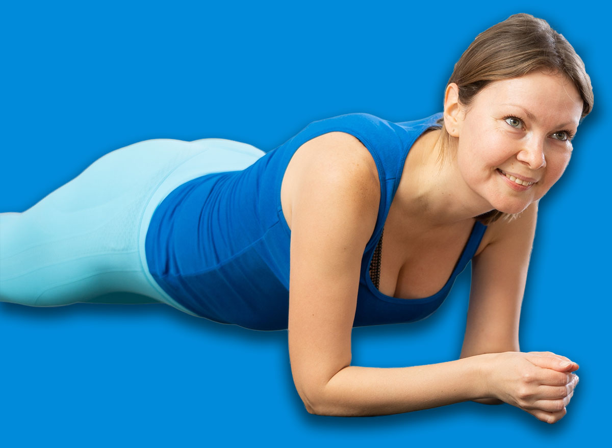 Diligent women practicing plank pose of yoga on black mat in light fitness room with house plants