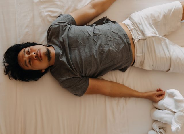 Sleepy lazy asian man do not want to get up from the bed.