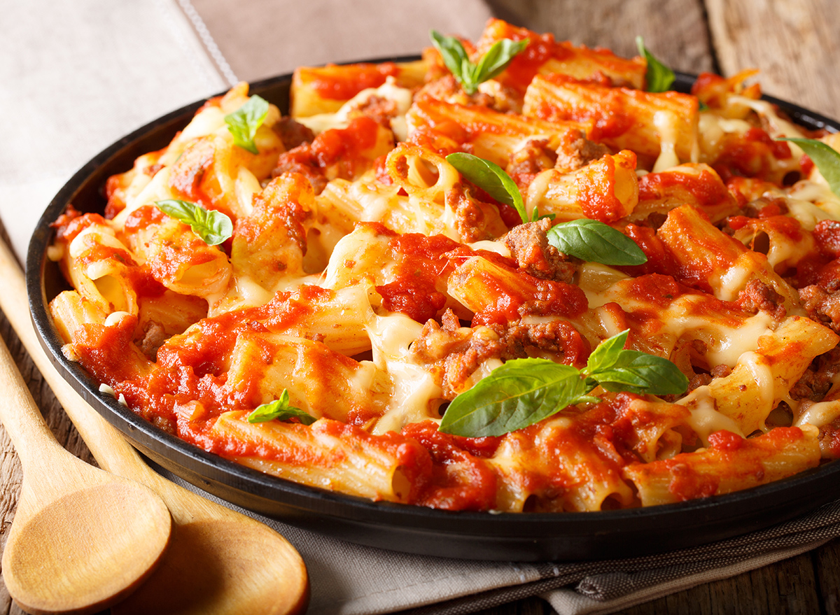 Spicy pasta ziti with minced meat, tomatoes, herbs and cheese close-up on a plate. horizontal