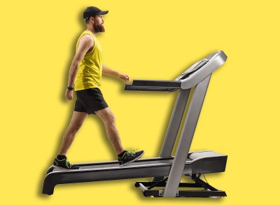 Full length profile shot of a bearded guy in sportswear walking on a treadmill with an incline isolated on white background