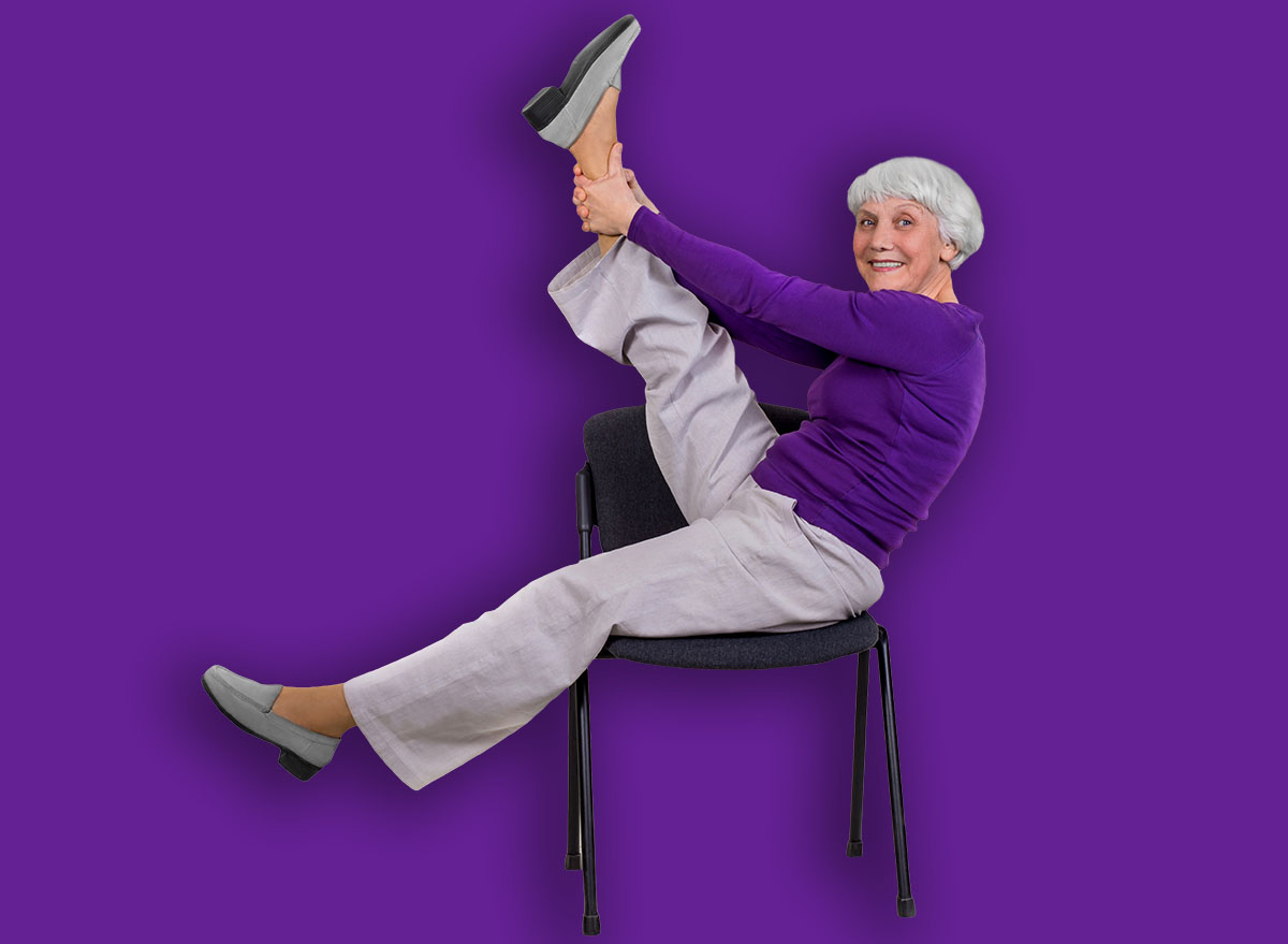 Happy charming beautiful elderly woman is doing exercise on a chair. Exercising gymnastics for health in the fitness room. Sports training.