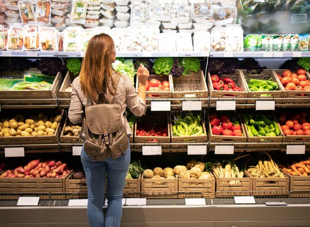 Good looking woman standing in front of vegetable shelves choosing what to buy. Buying groceries and healthy organic food in supermarket.