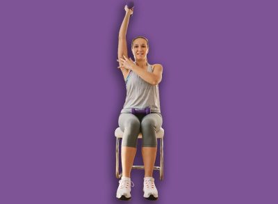 Muscular sportswoman in shape sitting on the chair at home, lifting dumbbell and showing biceps with other hand.
