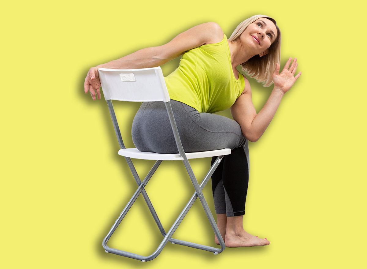 Yoga with a chair. Adult caucasian woman sits and practice side twists with props on a mat in loft white studio indoor, selective focus.