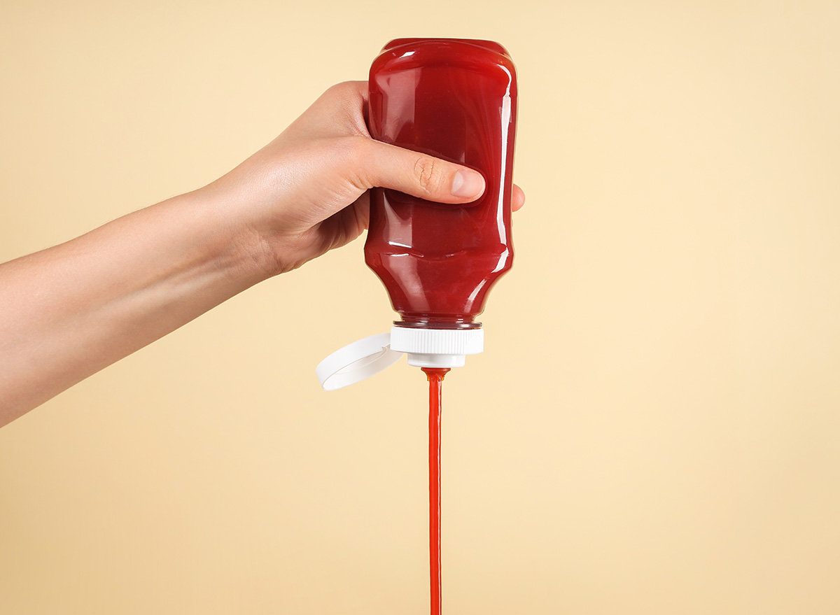 Woman pouring tasty ketchup from bottle on beige background, closeup. Space for text