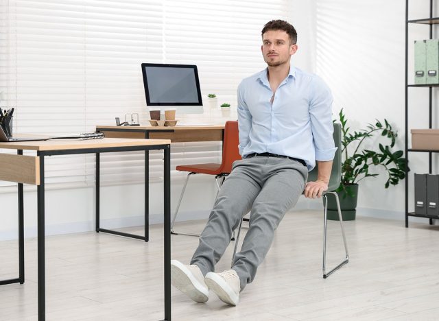 Handsome man exercising with chair in office