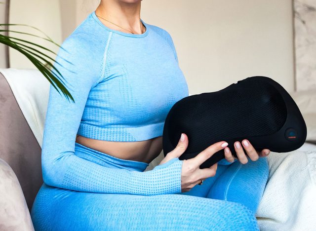 In a serene indoor environment, woman is holding a neck massage pillow while seated comfortably. This scene captures the essence of self-care and relaxation after sports exercises. Copy ad text space