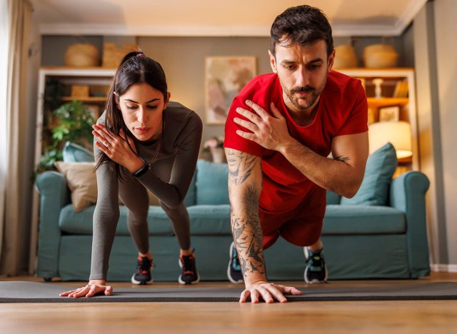 Active fit couple in sportswear doing plank shoulder taps exercise while working out together at home