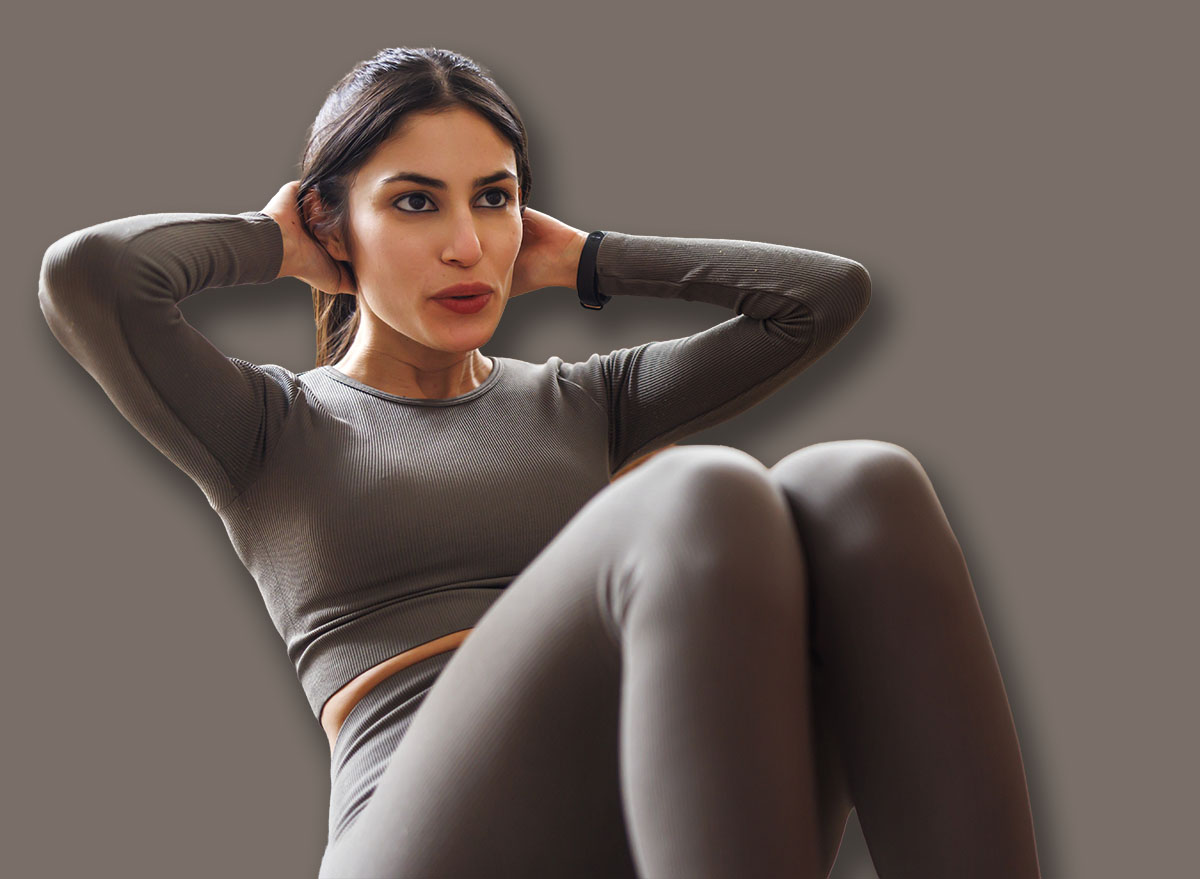 Active couple in sportswear doing home workout - man holding woman's legs assisting her while doing sit ups