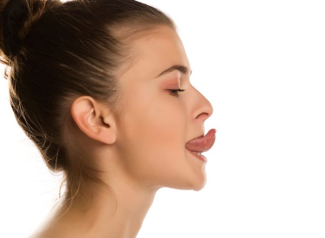 Young woman trying to touch the nose with her tougue on white background