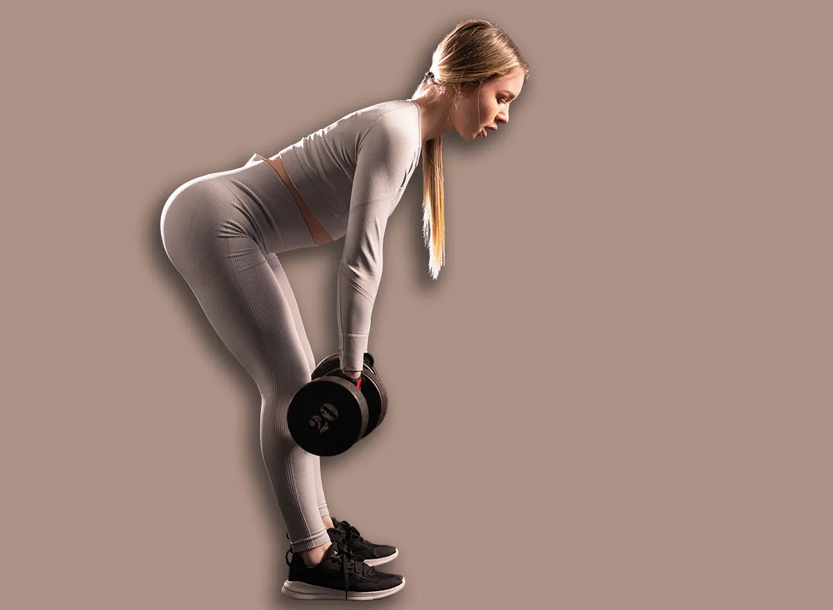 Fitness girl with a good figure in tight sportswear is training in the gym. exercise with dumbbells deadlift, back strengthening. Sport and fitness concept.