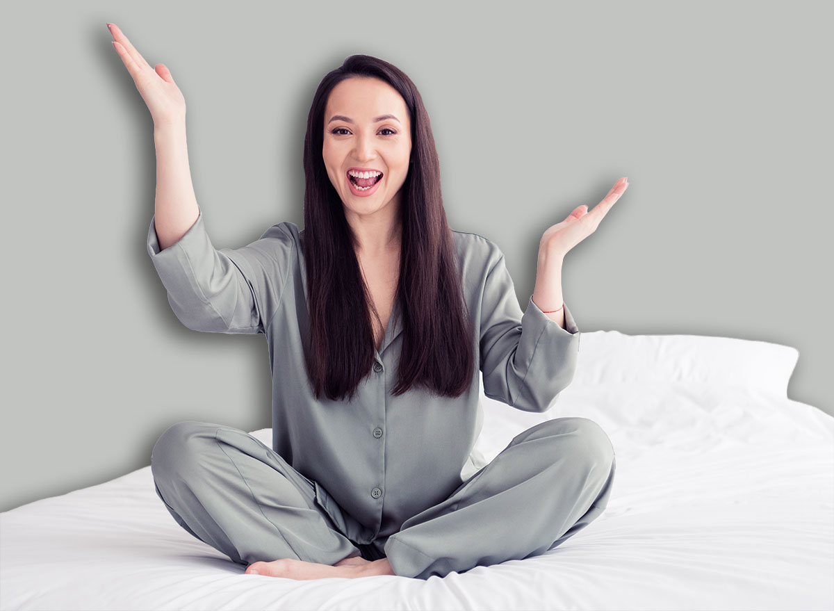Photo portrait of attractive young woman sit soft bed raise hands excited wear trendy gray pajama isolated on white modern interior design
