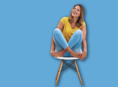 Woman, portrait and relax by blue wall with chair for leisure, calm and positive attitude on weekend. Female person, face and chill on seat with barefoot or feet for comfort, peace and playful mood