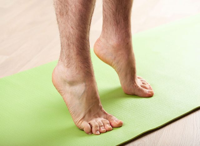 man doing flatfoot correction gymnastic exercise standing on toes at home