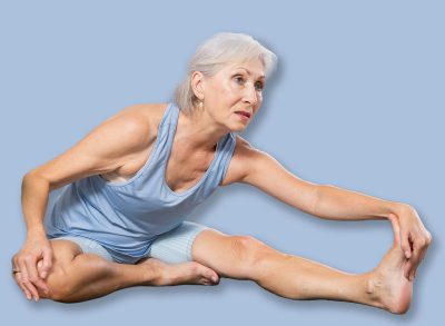Sporty senior woman practicing yoga with group in modern studio, performing Janu Sirsasana seated asana to stretch hamstrings, back muscles, and spine