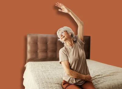 A happy senior woman sitting on a bed at home and doing senior fitness exercises.