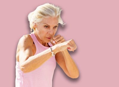Mature woman doing sport in a coastal port. Arm training throwing boxing punches. Female doing shadow boxing outdoors.
