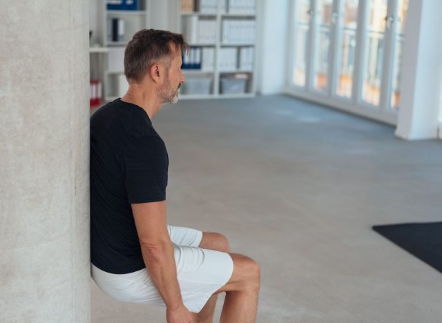Fit healthy man doing a wall leg sit or squat in an office gym to strengthen and tone his muscles in an active lifestyle concept with copy space