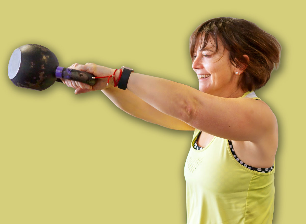 Mature woman performing a kettlebell swing exercise, focusing on fitness and strength training