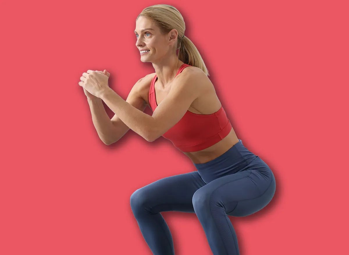 Athletic woman doing squats with fitness elastic band on mat at home