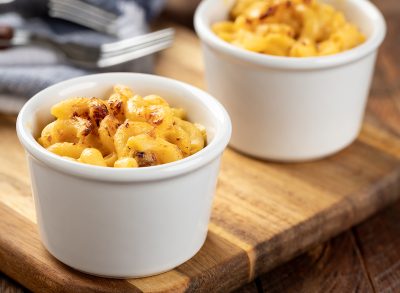 Baked macaroni and cheese in a white cup on a wooden board