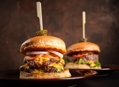 Double cheese burgers on brown dish with dark background.