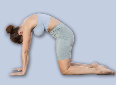 Portrait of caucasian woman standing on sports mat and making yoga meditation in cat-cow pose of yoga on beach at morning outdoors