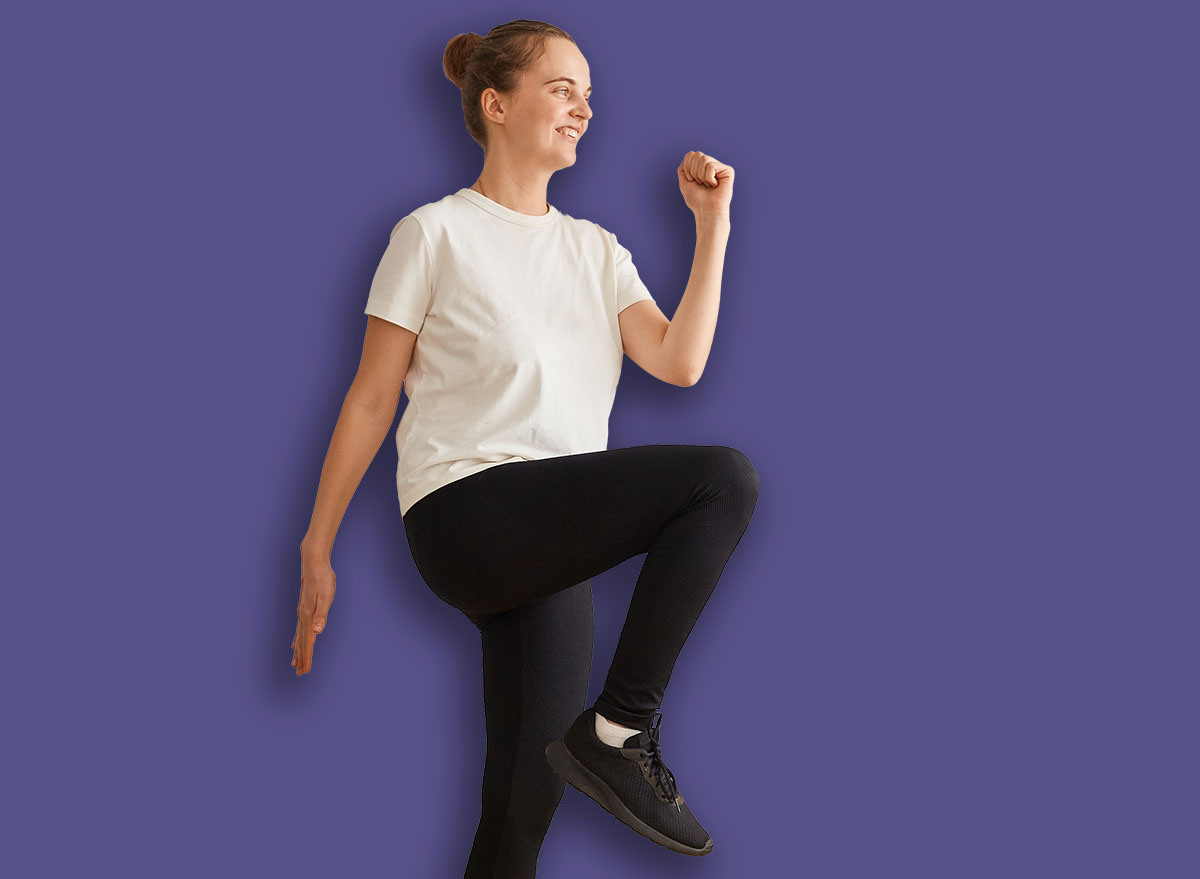 Full length portrait of slim athletic woman wearing white t shirt and black leggins doing sport exercises at home on yoga mat, walking in place, marching, sport, fitness at home.