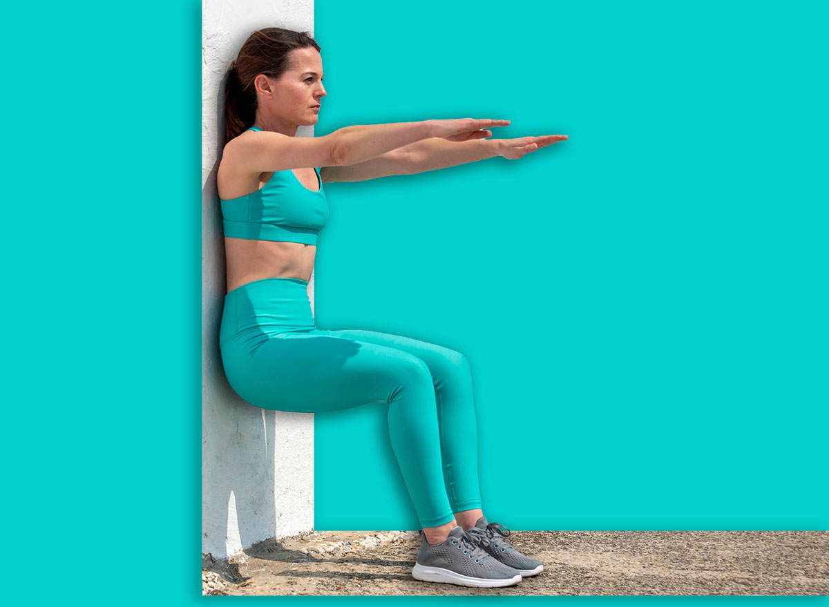 Sporty woman doing squats against a white wall outside in the sun.