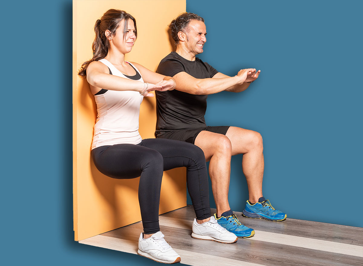 Athete people doing squats leaning on wall in gym