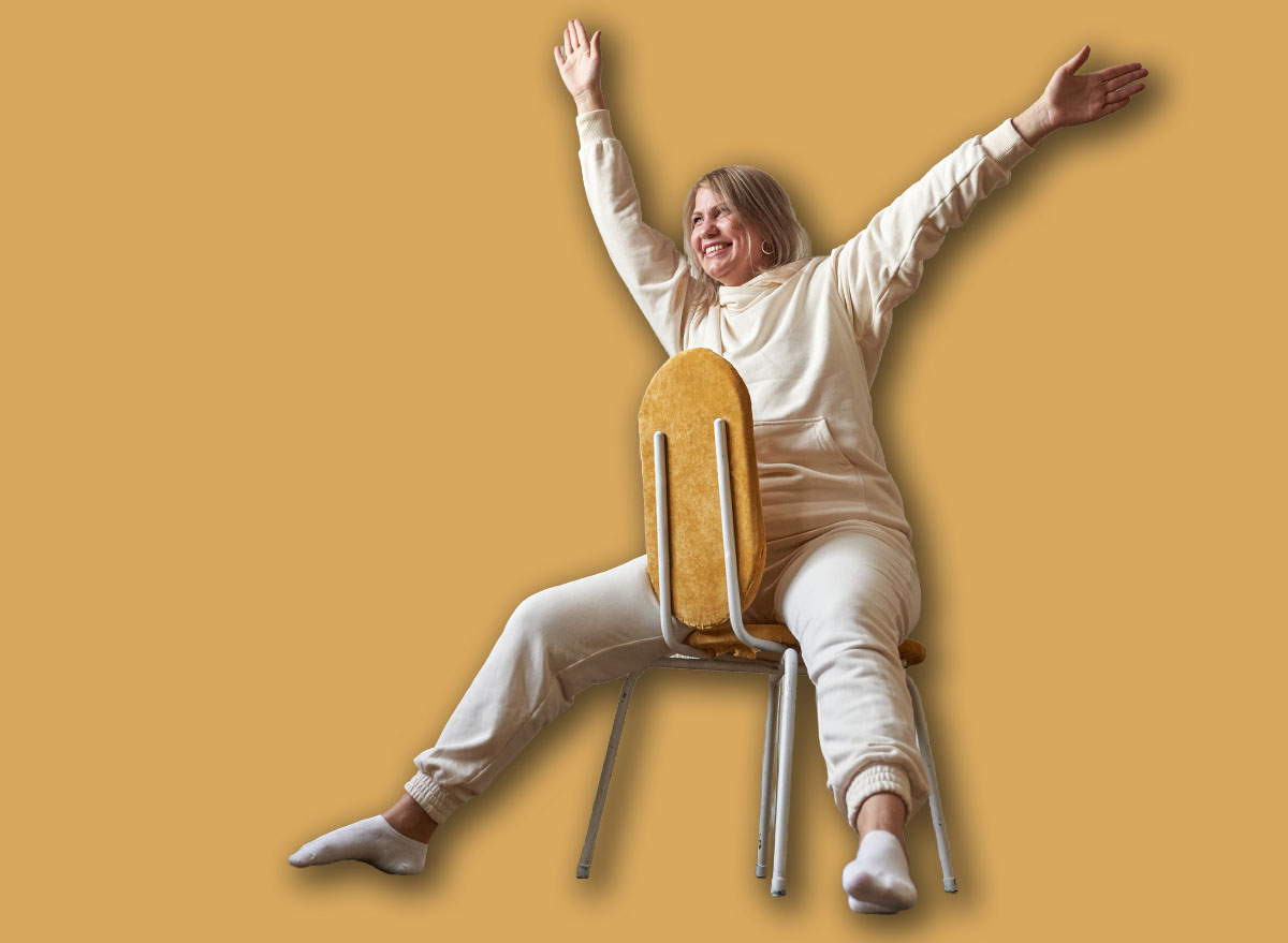 Caucasian young female performing chair exercise with joyful expression in bright room.