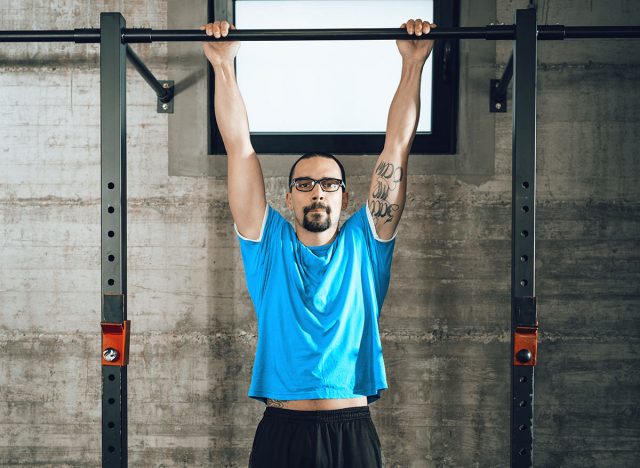 Handsome young muscular man doing pull-ups exercise at the gym. Looking at camera.