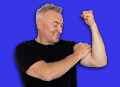 Senior man showing biceps. Male model in black T-shirt showing off biceps with smile. Portrait, studio shot, health concept