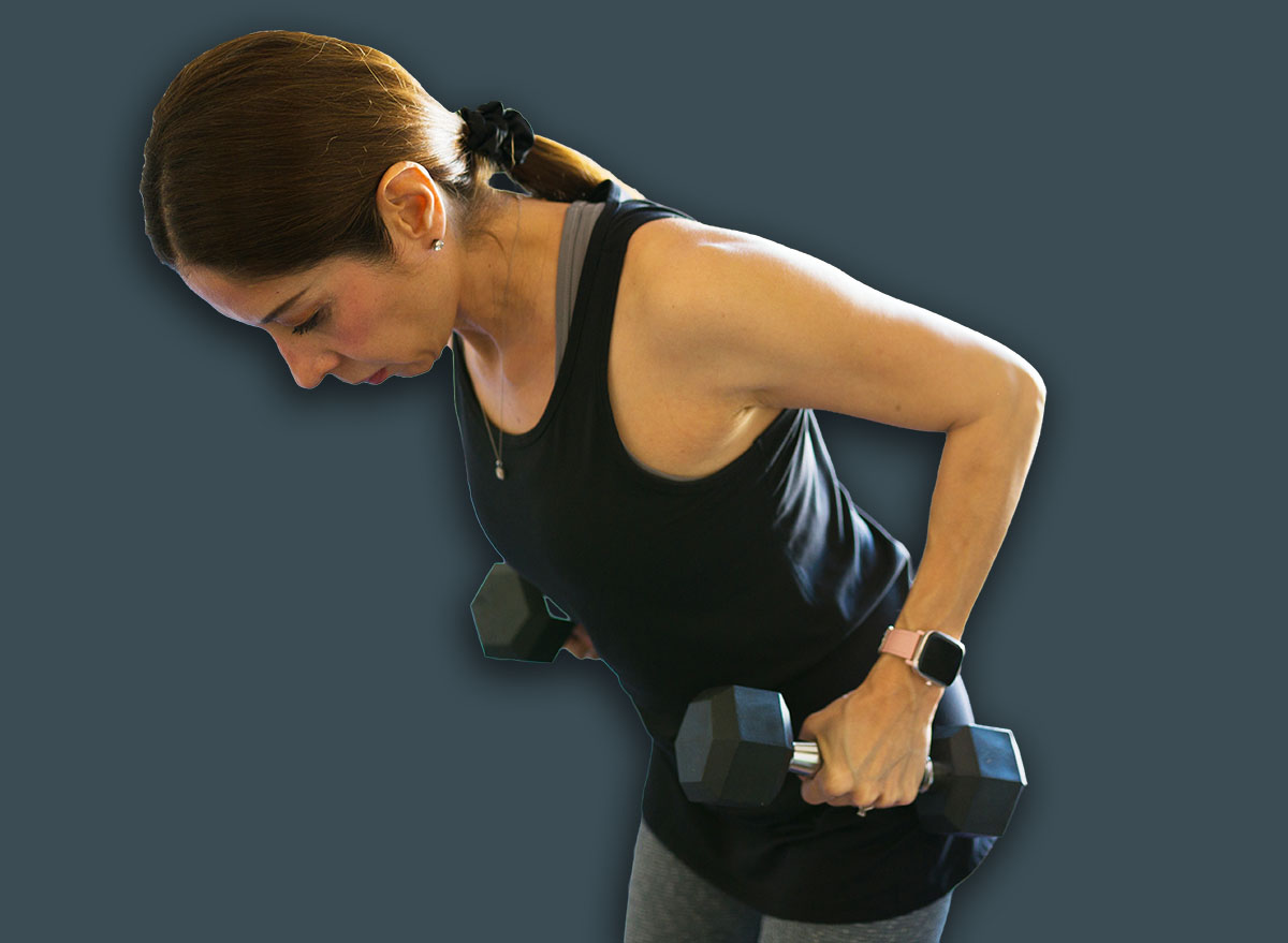 Fit mature woman is using free weights to exercise in her bedroom, determined to stay fit and strengthen her muscles through her workout routine