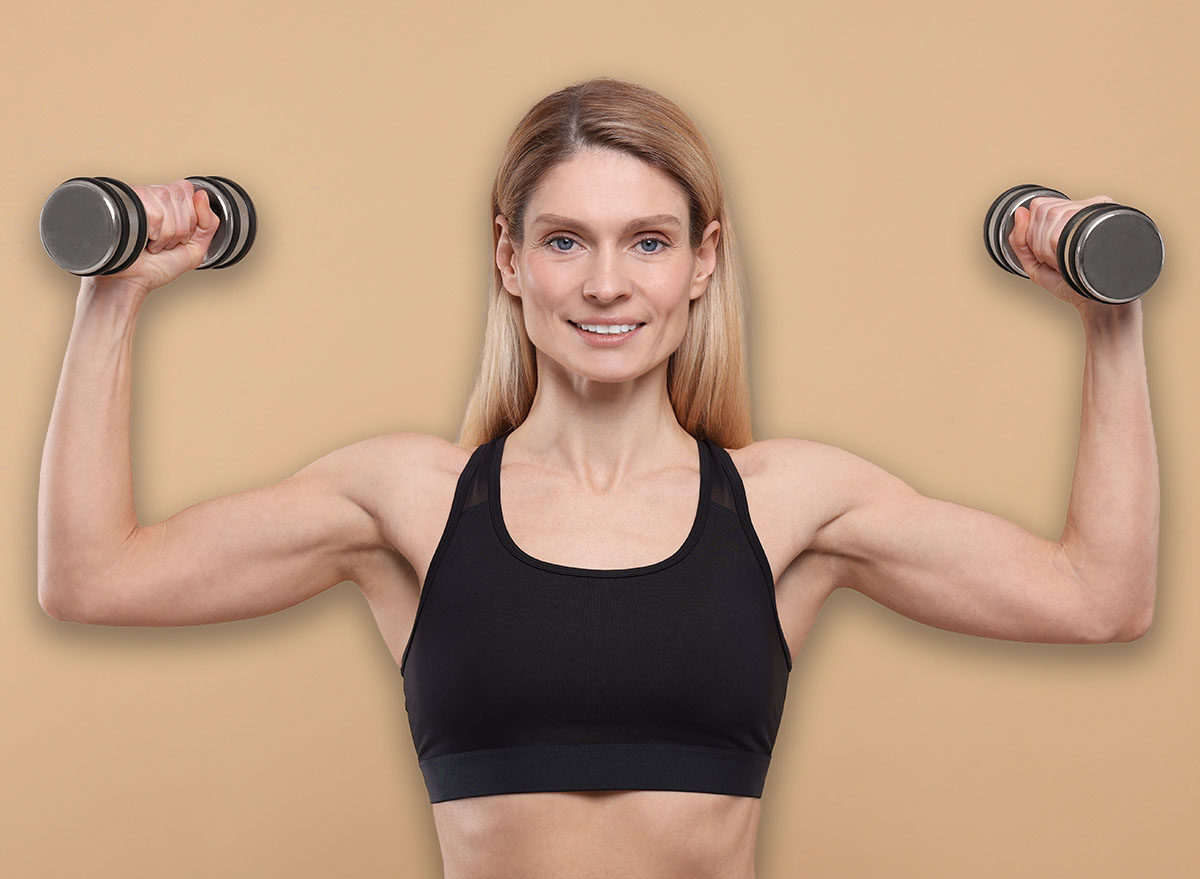 Portrait of athletic woman exercising with dumbbells on beige background