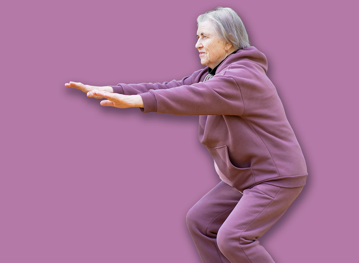 A mature happy woman in a purple tracksuit doing a half squat outdoors. Performs exercises in the autumn park. Full length portrait.